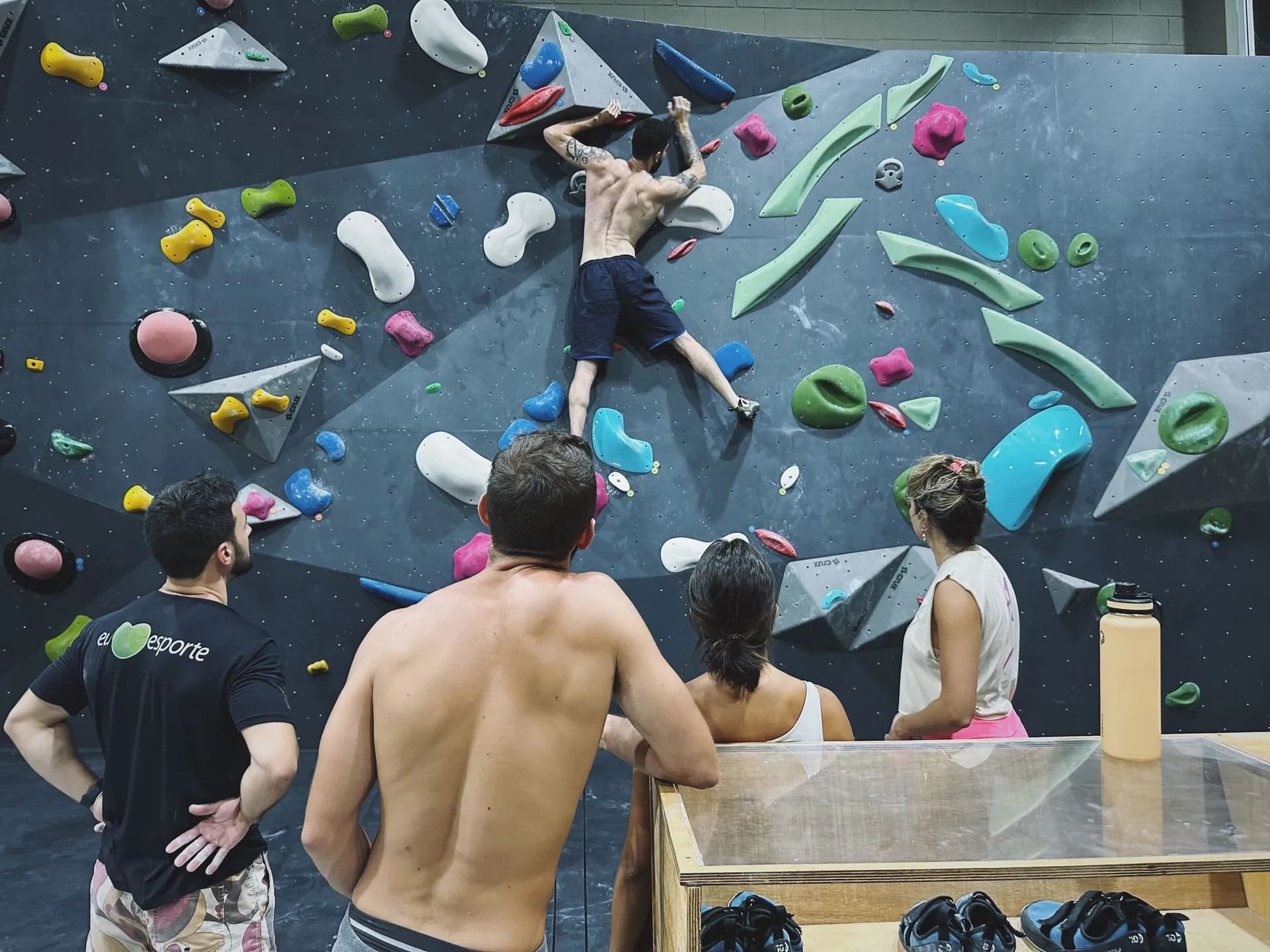 Escalador na parede de boulder da Geometrik, com a galera acompanhando os movimentos