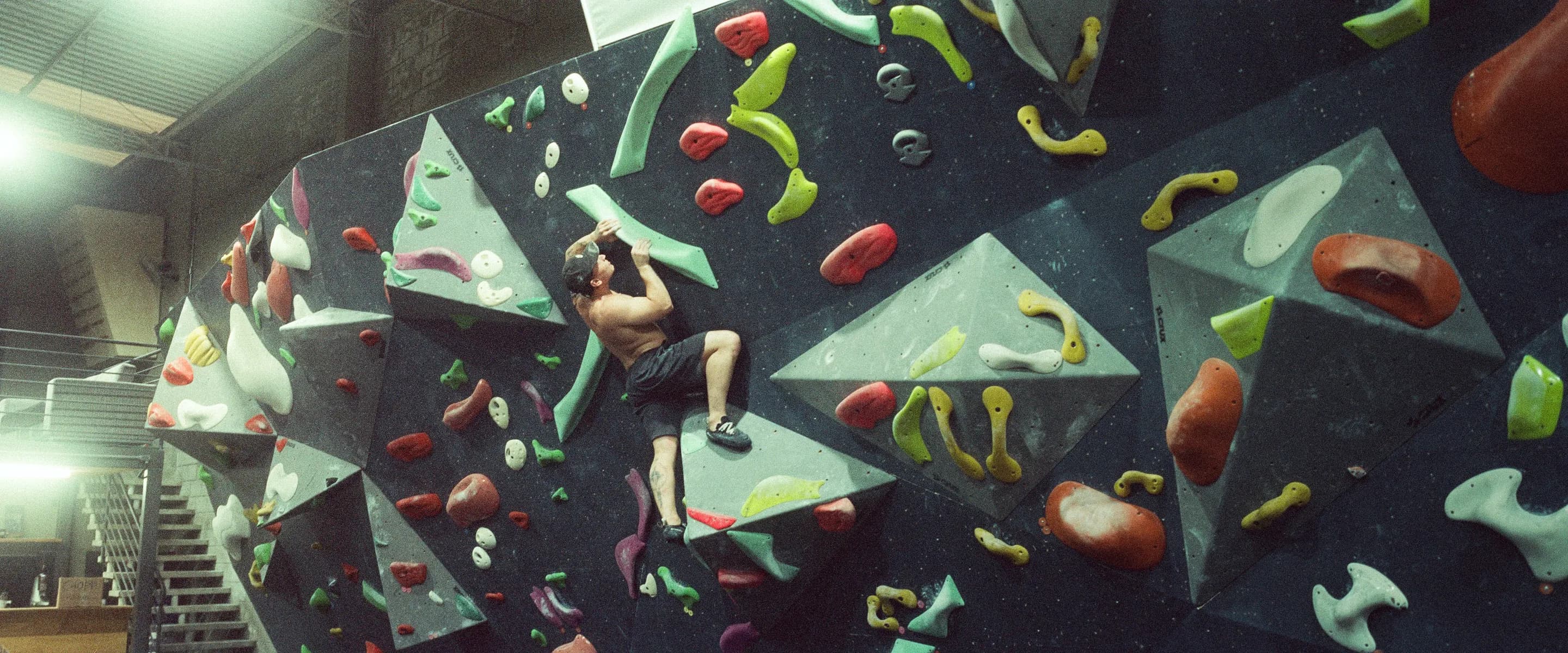 Escalador subindo uma parede de boulder com agarras coloridas na Geometrik